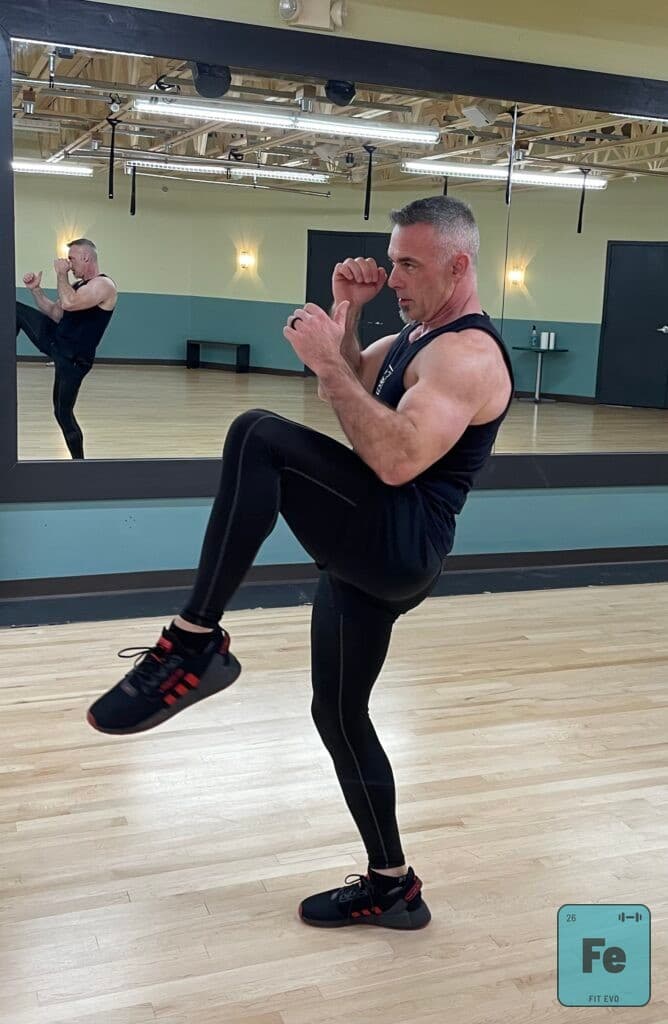 An instructor driving a knee upward with both fists raised in guard.