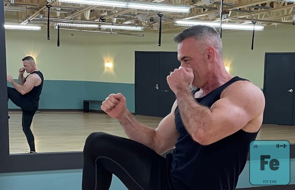 A cardio kickboxing session at FIT EVO, a member driving a knee upward with both fists raised in guard.