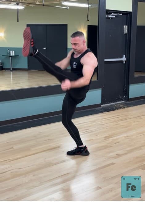 An instructor delivering a high front kick during a cardio kickboxing demonstration.