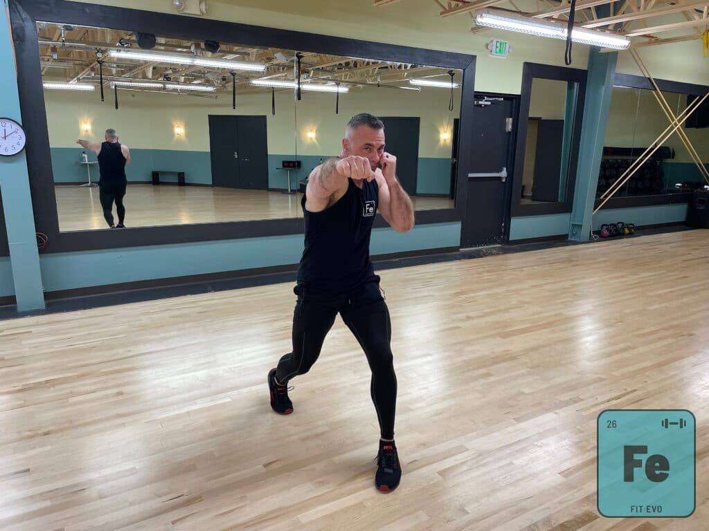 An instructor holding a boxing guard in front of the studio mirror.