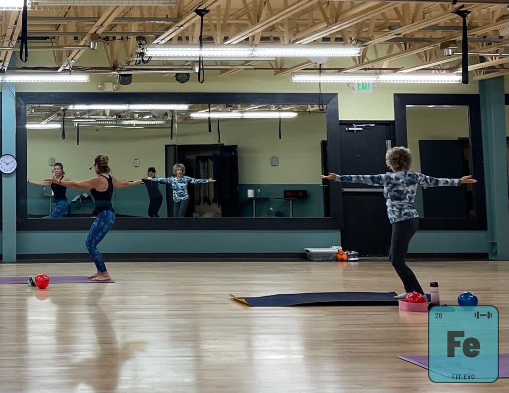 Members standing with arms extended during a balance exercise in the studio.