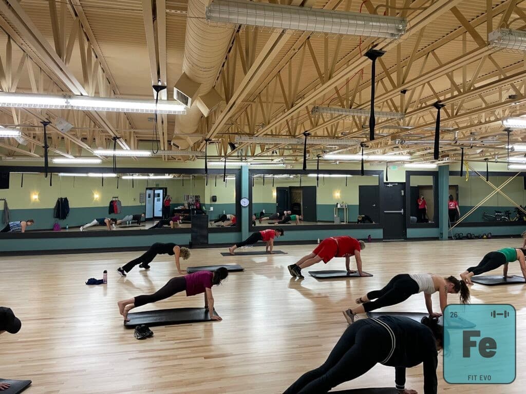 A mat class in the FIT EVO studio, members holding a plank position on their mats in rows facing the mirrored wall.