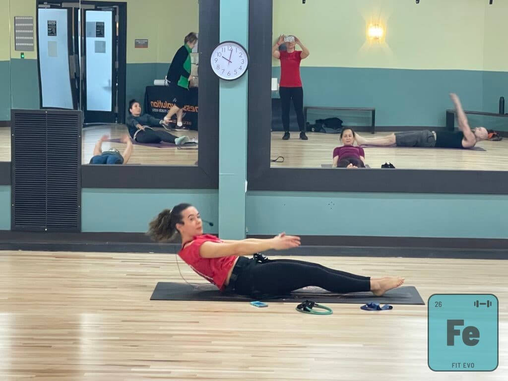 A member performing a seated roll-back on a mat during a class.