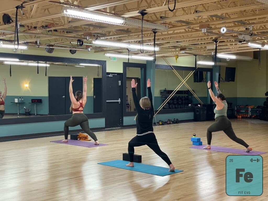 A yoga class holding warrior pose with arms overhead.