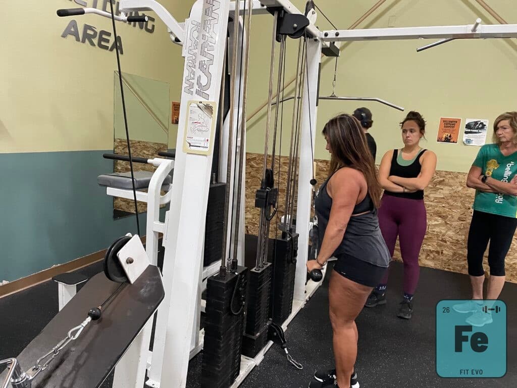 A trainer demonstrating a cable machine to a small group in the FIT EVO stretching area.