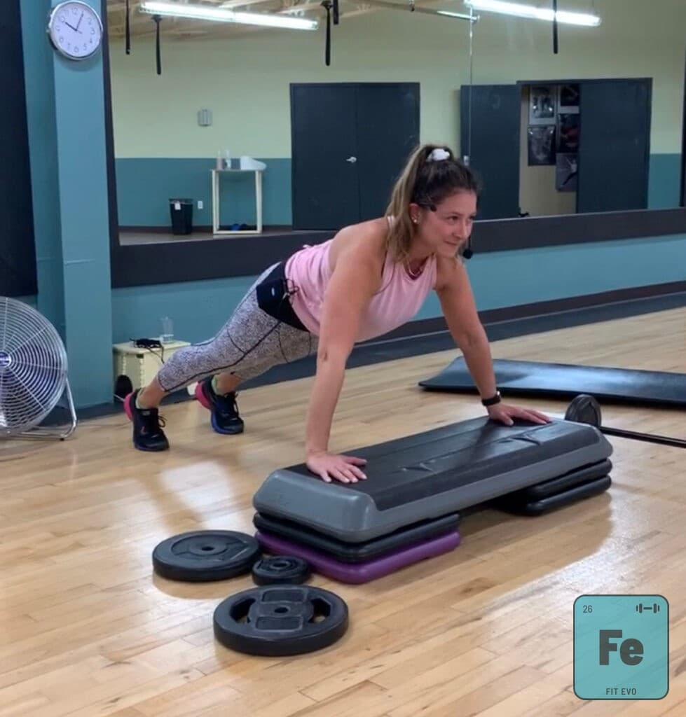 A member performing an incline push-up with hands on a step platform.