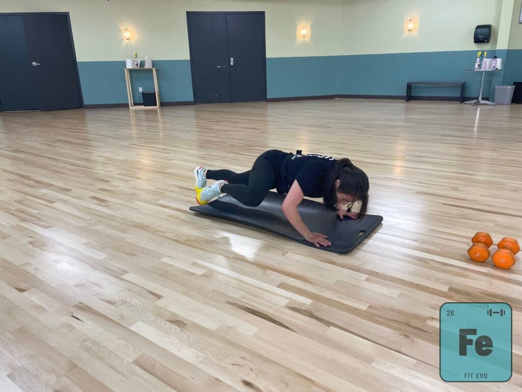 An instructor holding a low plank on a mat in the FIT EVO studio.