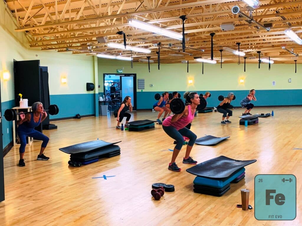 A strength class in the FIT EVO studio training with weighted bars and step platforms.