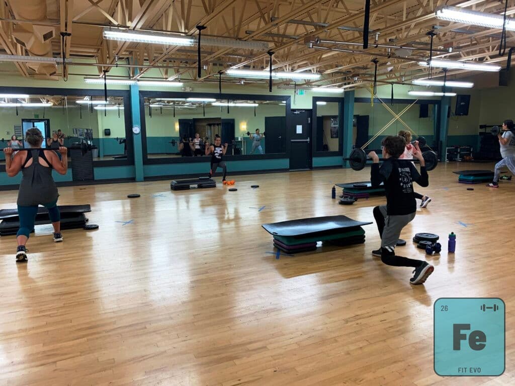 Members performing barbell squats and lunges during a class.