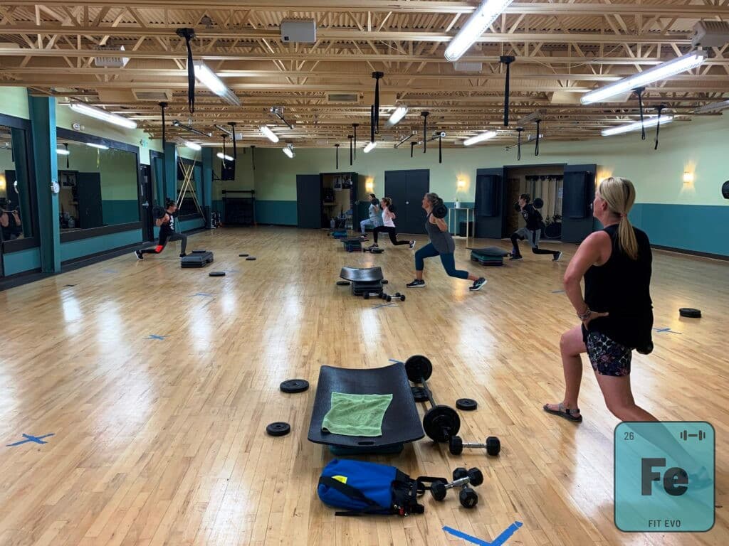 A group class in the FIT EVO studio working with steps, dumbbells and weight plates.