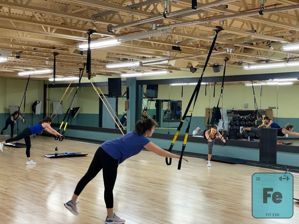 A TRX suspension training class in the FIT EVO studio, straps hanging from ceiling anchors as members lean back into a row.