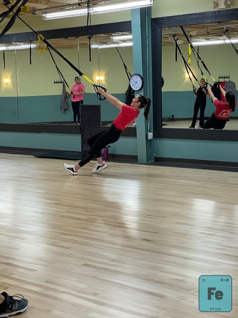 A member leaning back into TRX straps to perform a row.
