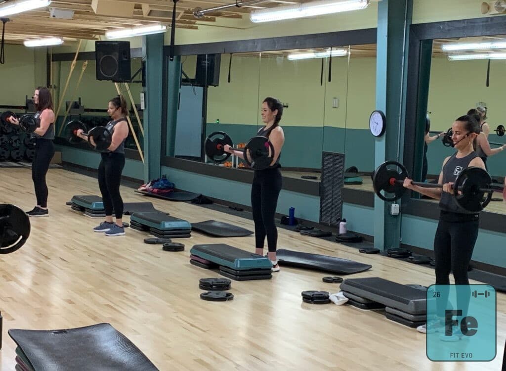 Members performing barbell curls in front of the studio mirror.