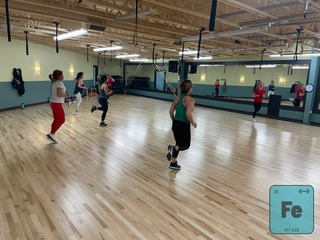 A cardio class driving knees upward across the studio floor.