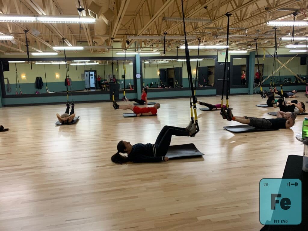 Members lying on mats working with TRX straps during a class.