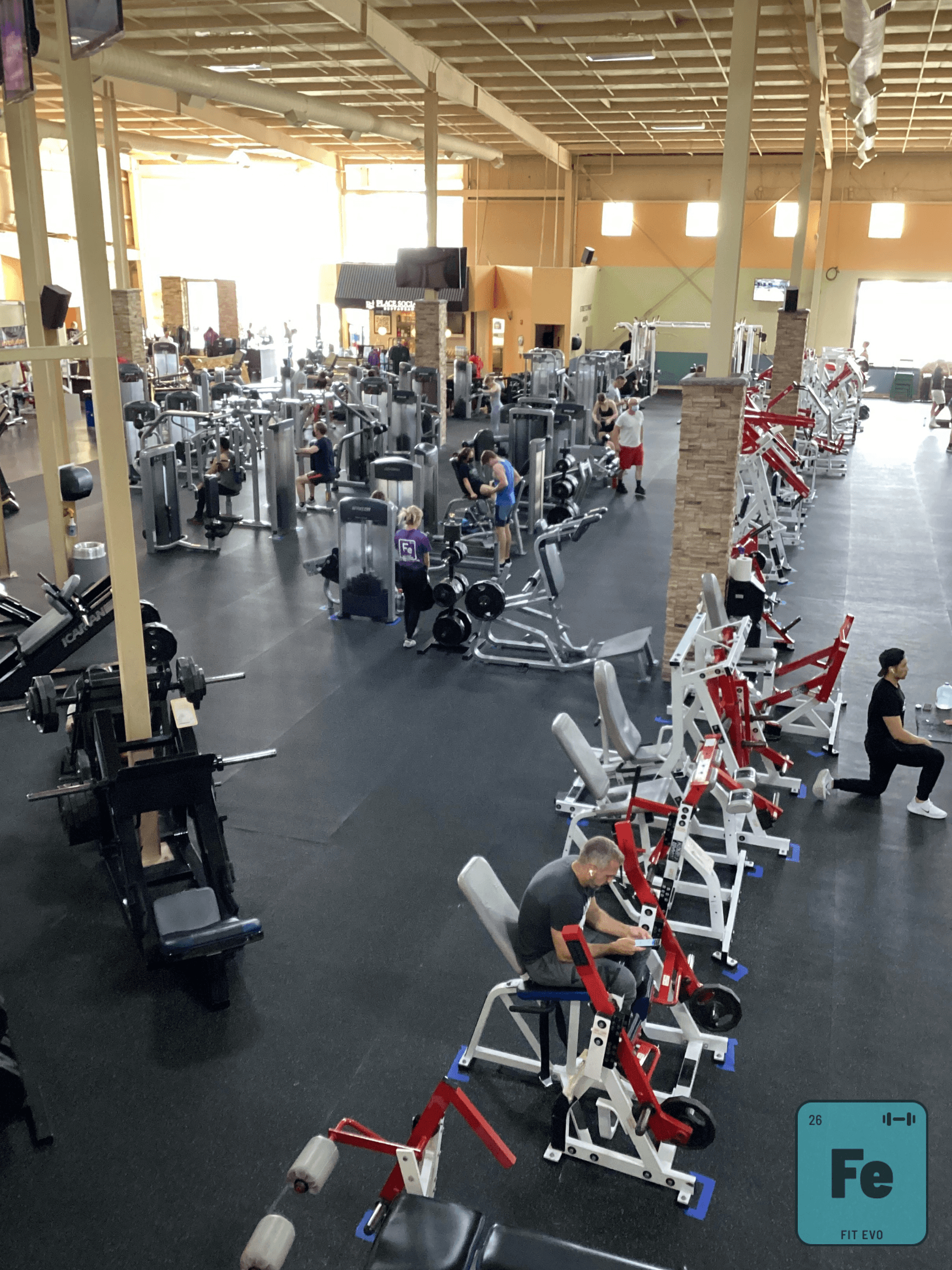 A wide view across the FIT EVO gym floor, showing long rows of plate-loaded and selectorised weight machines with members training between them.