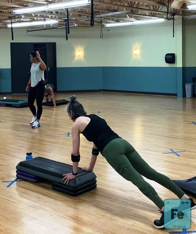 A member holding a plank with hands on a step platform.