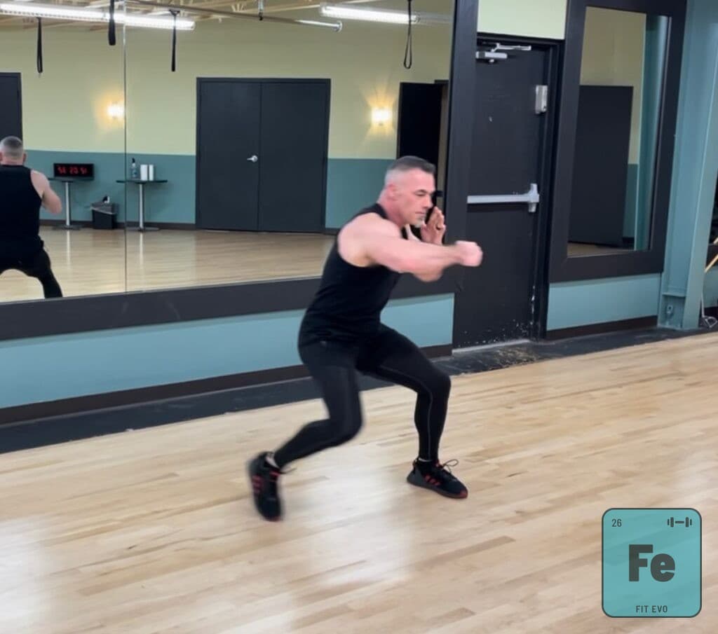 An instructor dropping into a low boxing stance in front of the studio mirror.