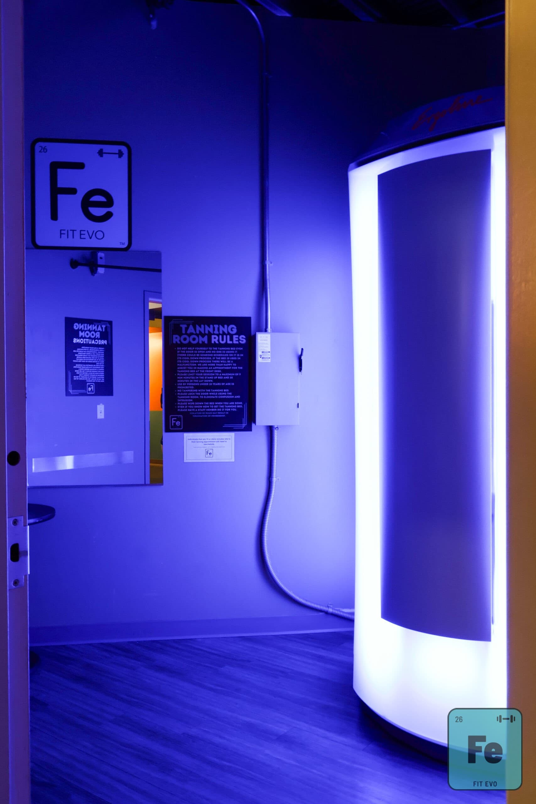 A stand-up tanning booth at FIT EVO, beside the posted tanning room rules.