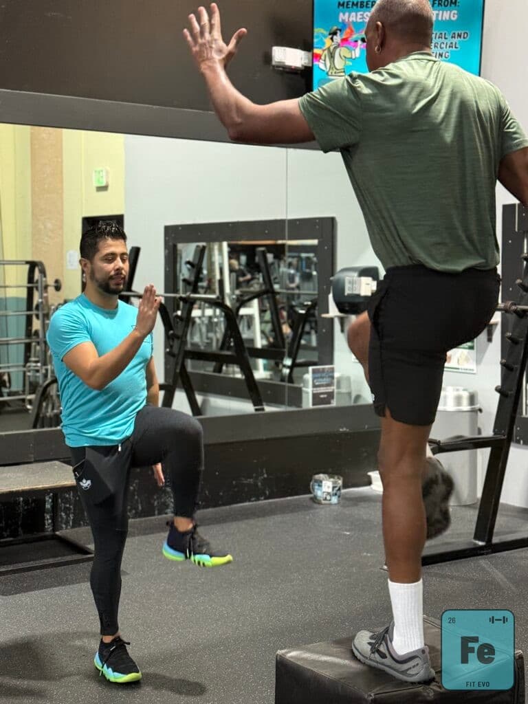 A trainer guiding a member through a standing balance exercise.