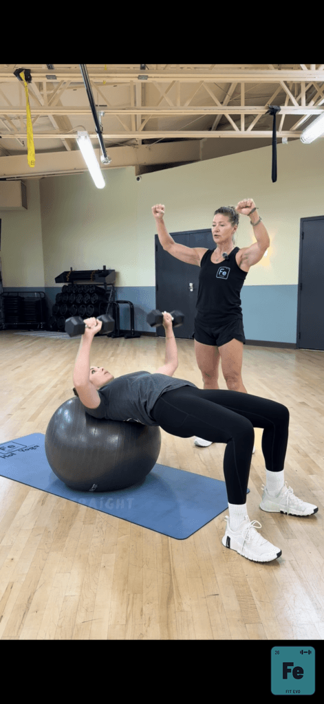 A trainer supervising a member stretching back over a stability ball.