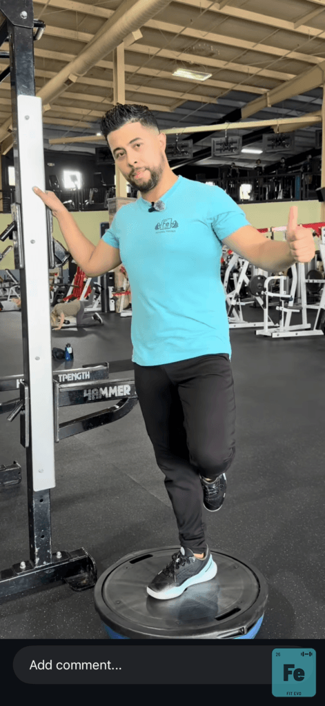 A trainer demonstrating a balance exercise on the FIT EVO gym floor.