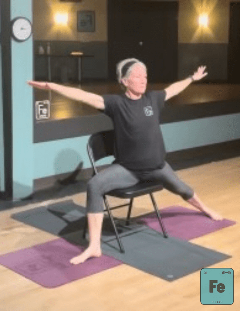 A participant in a seated chair yoga class with arms extended.