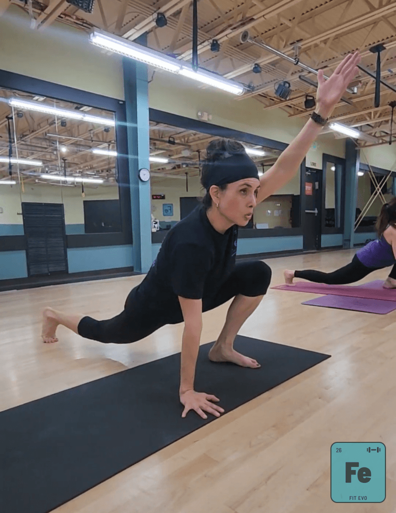A member holding a low lunge with one arm raised during a yoga class.