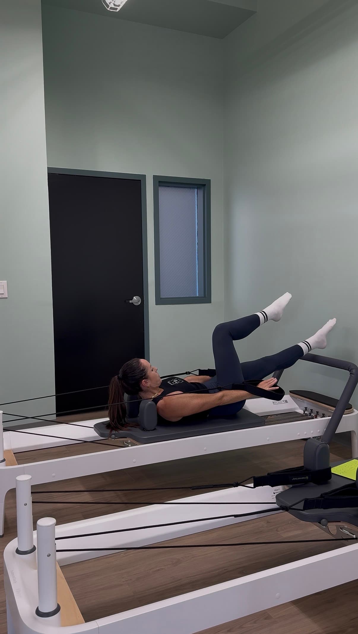 A Fit Evo instructor lying back on the reformer carriage with both legs raised, working against the springs