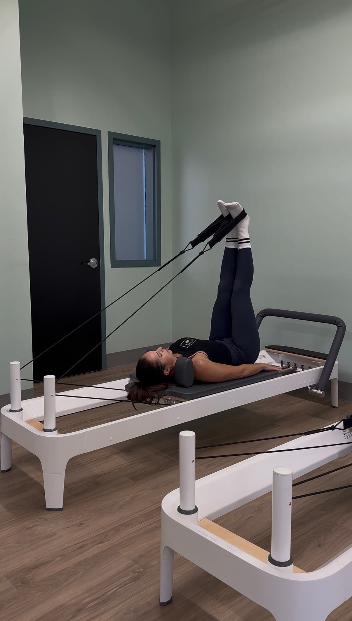 Two Pilates reformers in the Fit Evo studio, one in use with the foot straps raised overhead